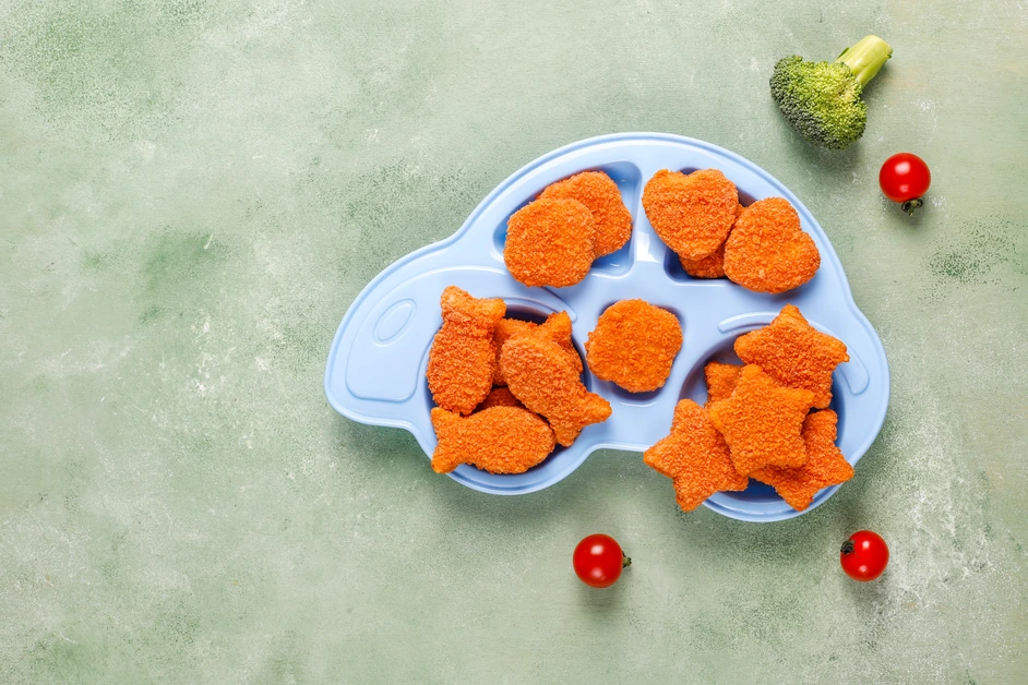 Golden crispy chicken nuggets served with ketchup and a side of fries on a wooden tray.