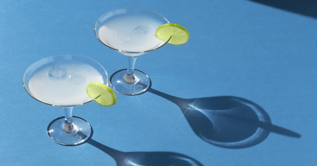 A bartender serving a margarita cocktail with a lime wedge and salt rim.