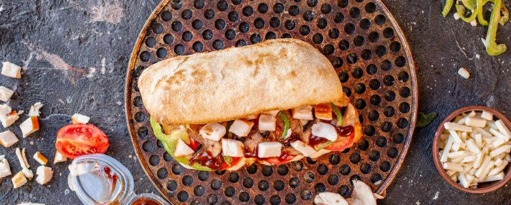 Stacked chicken cutlet sandwich with layers of lettuce, tomato, and creamy mayo on a cutting board.