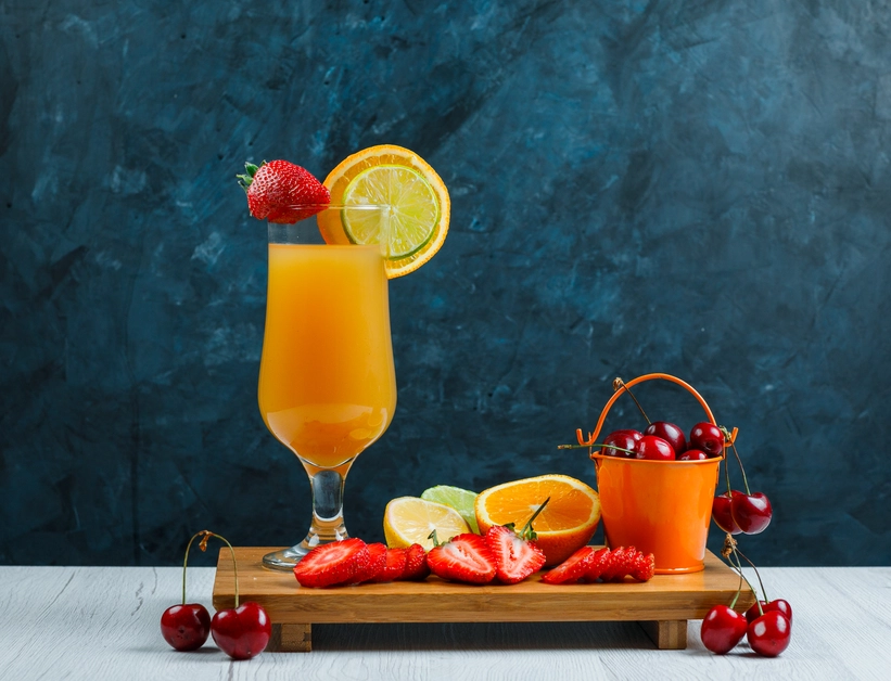 Four colorful jars of Happy Juice on a rustic wooden tray, surrounded by lemons, limes, and pomegranate seeds for decoration.