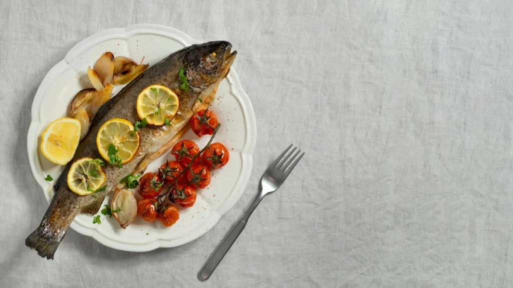 Whole Loup de Mer grilled on a platter with garnished herbs and lemon slices.