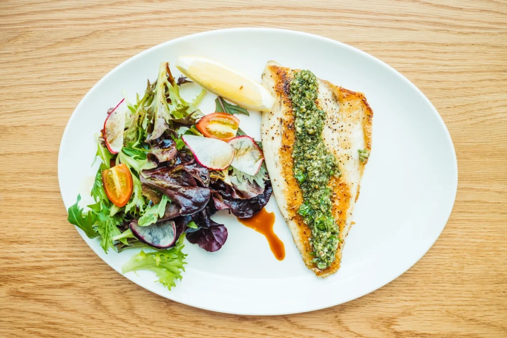 Golden-brown breaded sand dabs served with a side of tartar sauce and a wedge of lemon on a rustic wooden table.