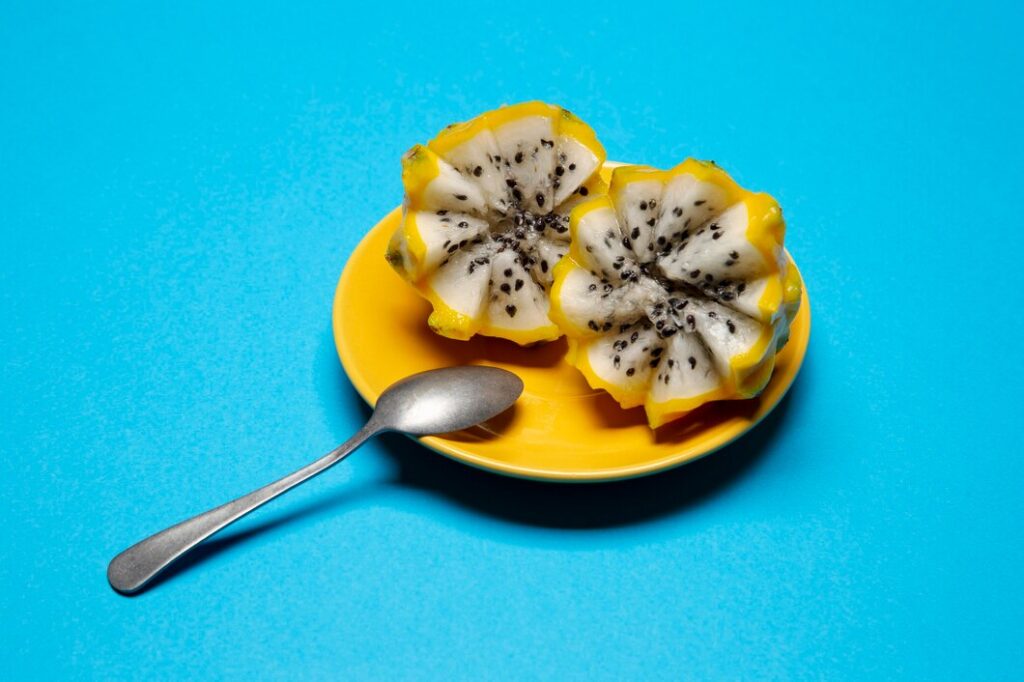 A whole yellow dragon fruit resting on a wooden surface with its spiky outer skin and bright yellow color.