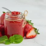 Fresh strawberry puree in a glass jar with strawberries around it
